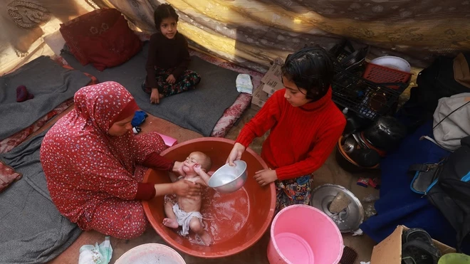 Một phụ nữ Palestine tắm cho con trong căn lều ở khu trại tị nạn ở Rafah, miền Nam Gaza ngày 18/1/2024. (Ảnh: AFP)